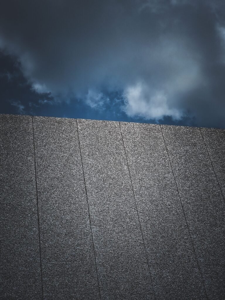 A low angle view of a modern building wall against a dramatic cloudy sky, showcasing urban architecture.